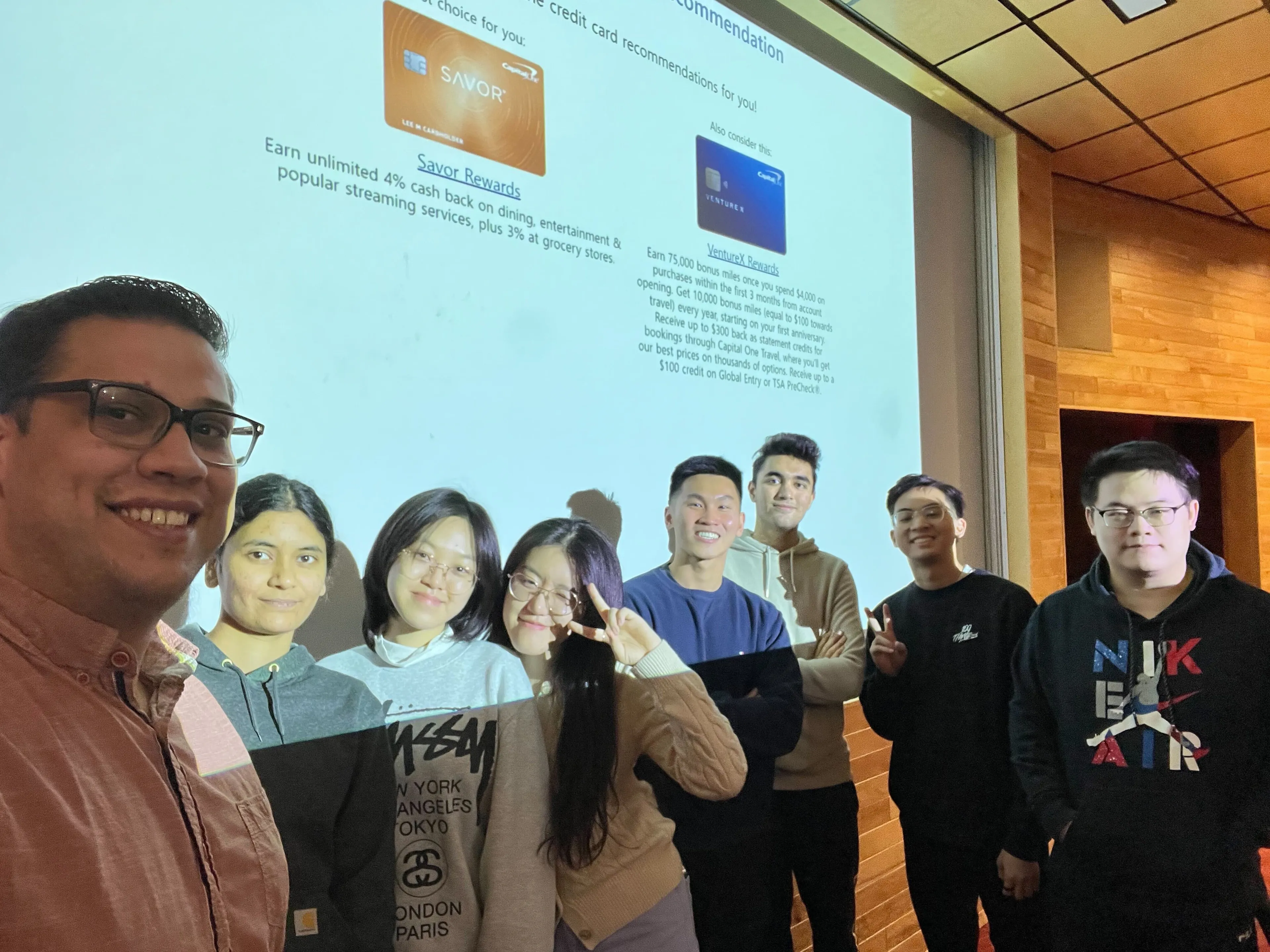 Eight project team members smiling for a selfie in front of a projected Savor Rewards recommendation in a lecture hall